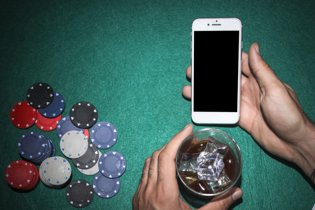tangan menunjukkan ponsel dan memegang segelas minuman dengan chip poker di atas meja
